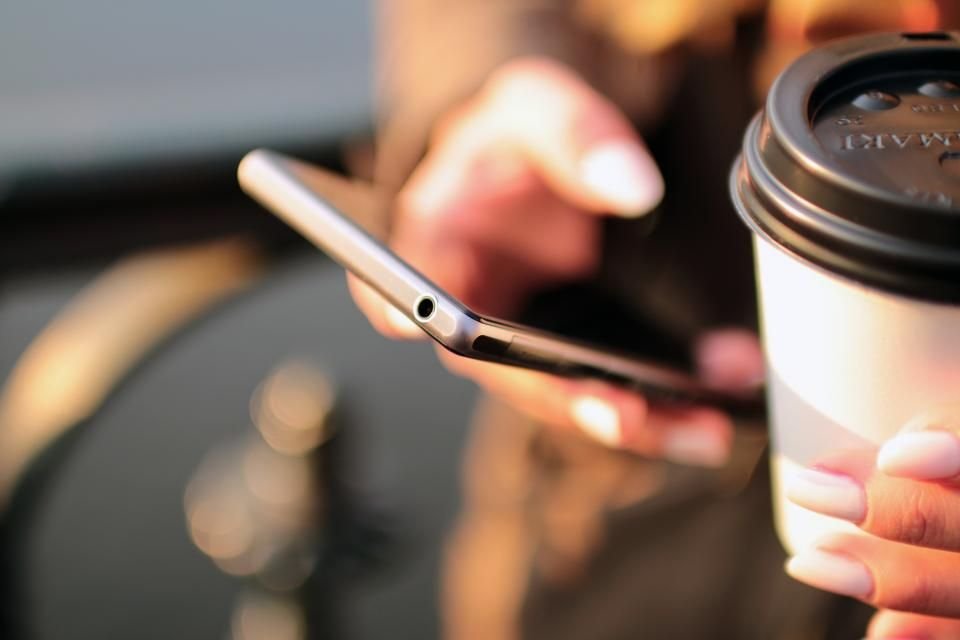 Persona usando el móvil con un café al lado