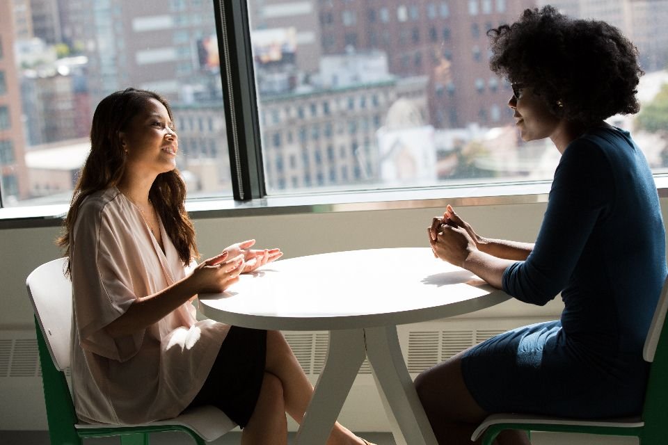 Dos amigas conversando en una mesa junto a una ventana